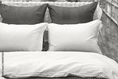 Comfortable bedding display with white and dark pillows on wooden flooring in a cozy bedroom setting.