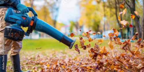 Worker using a leaf blower to clear fall leaves in a park