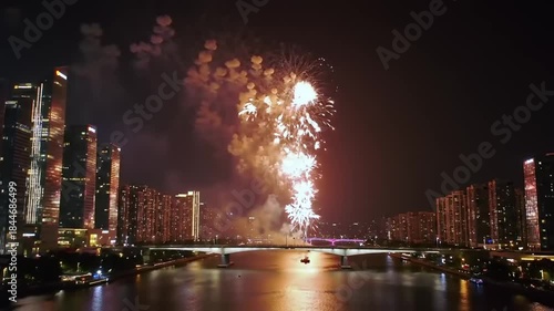 Nighttime fireworks display over cityscape and river reflecting lights