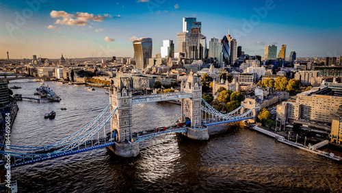 Aerial view of Tower Bridge over the River Thames with London’s modern skyline glowing in warm daylight. A striking mix of historic architecture and contemporary cityscape.