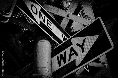 Obraz na plátně Black and white urban street signs showing one way direction under a metal structure