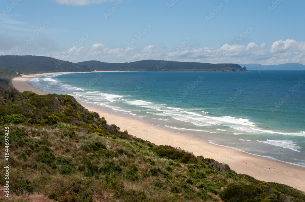 Obraz premium Bruny Island coastal landscape with long sandy beach, gentle waves and green hills, showing remote Tasmanian shoreline and natural ocean environment.