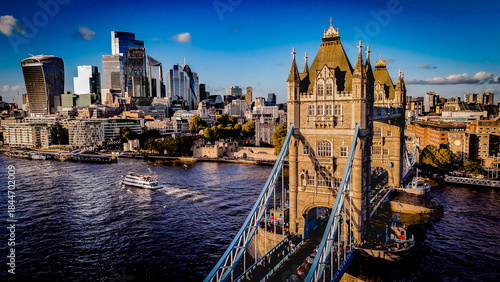 Obraz na plátně Tower Bridge captured from a low-angle perspective under clear blue skies, highlighting its iconic architecture and the modern London skyline in warm afternoon light