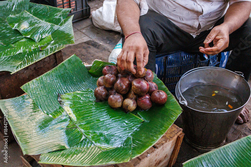 Vászonkép Indian street vendor arranging fresh jamun (java plum) fruits on banana leaves at a traditional market stall