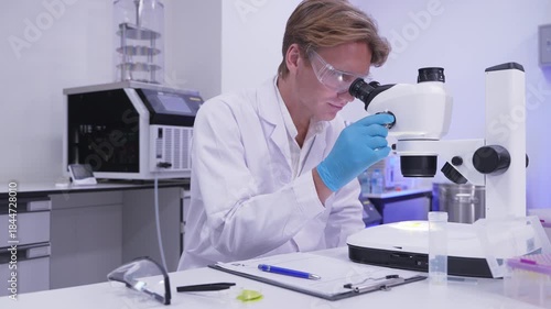 Scientist examines samples under microscope in laboratory setting focused on research work