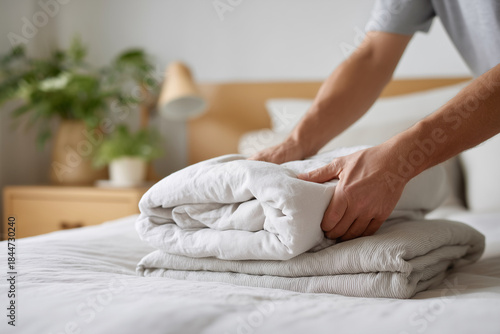 A man is folding a white sheet on a bed