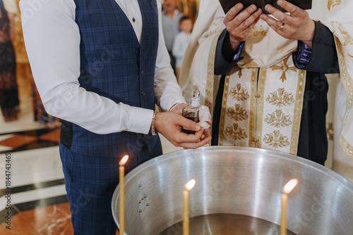 Fotografi Cropped shot of a man in a vest holding holy oil near a baptismal font with lit