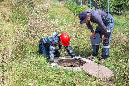 Workers inspect utility infrastructure, checking the meter and pipes in a water well in a rural area.