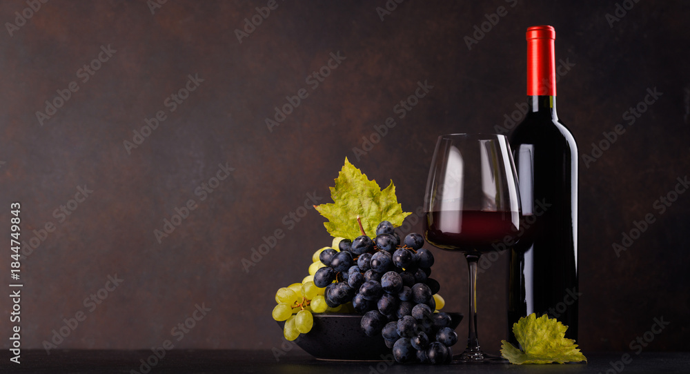 Obraz premium Red wine bottle with a glass and basket of fresh grapes