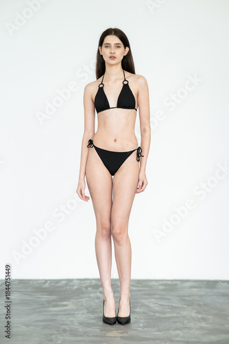 Young female fashion model in clean studio environment showing digitals and modelbook snaps for agency profile portfolio in bikini, frontal and profile angles	

