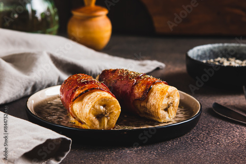 Baked banana roll with bacon on a plate on the table