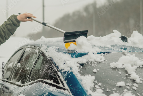 Cleaning Snow from a Car Hood with a Brush After Winter Snowfall
