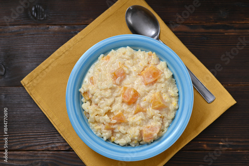 Pumpkin rice porridge in a bowl on a wooden table, flat lay