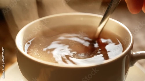 Close-up of Hand Stirring White Sugar into Hot Steaming Cup of Black Tea