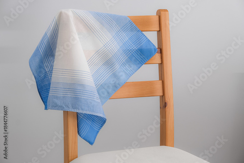 A classic blue and white patterned cotton handkerchief is draped over the backrest of a simple wooden chair against a plain gray background.