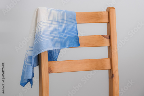 A classic blue and white patterned cotton handkerchief is draped over the backrest of a simple wooden chair against a plain gray background.
