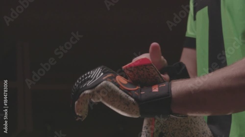 Close-up of an African American football player pulling up orange socks over his knees. The athlete is getting dressed and preparing for a soccer match in the locker room.

