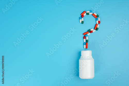 Question mark made of medicine capsules above bottle on blue background representing healthcare questions, medical uncertainty, treatment decisions, and pharmaceutical awareness concept.