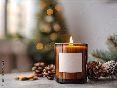 lit amber glass candle with empty white label on coffee table with pinecones gingerbread cookies and a Christmas tree glowing in background cozy interior lighting cin