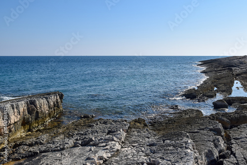 Fototapeta Naklejka Na Ścianę i Meble -  Rocky shoreline of Cape Kamenjak with its flat, layered limestone formations gently descending into the clear blue Adriatic Sea.