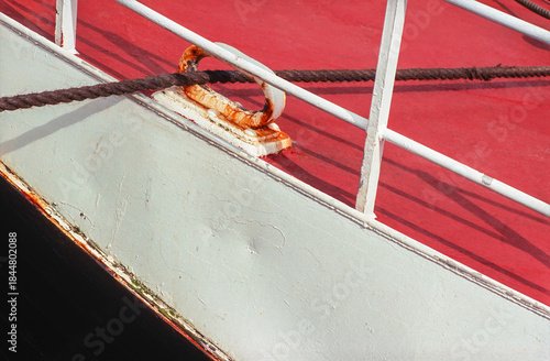 Detail of a rusty cleat and coiled rope on a boat’s weathered red deck showing signs of aging
