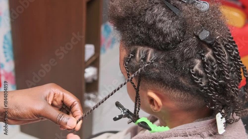 Close-up of stylist’s hands quickly finishing a braid on the side of teen boy’s afro hair