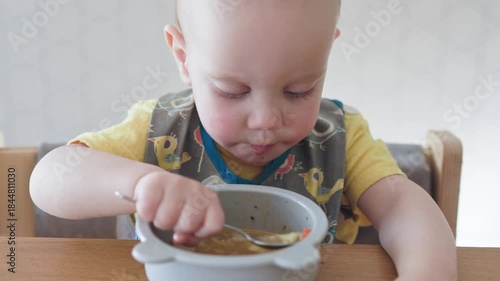 A joyful and delighted baby happily eating warm soup from a colorful bowl, showcasing beautiful mealtime moments