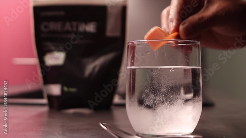 Close up of a hand scooping creatine monohydrate powder into a glass of water, stirring it with a spoon, preparing to boost muscle gain and energy before a workout