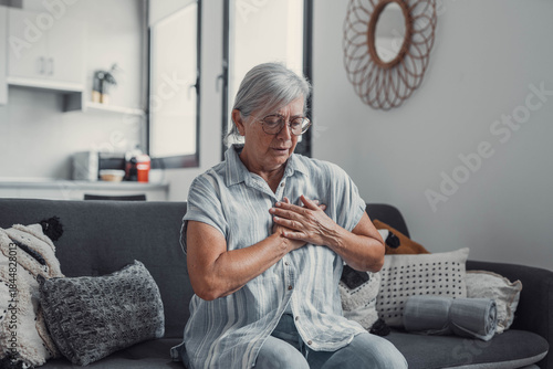 Foto Elderly woman sits on a sofa at home holding her chest in discomfort