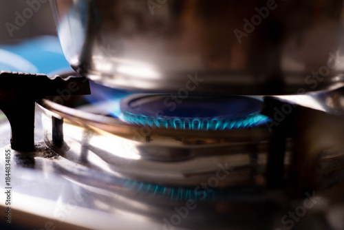 A close-up shot of a bright blue gas flame burning intensely under a reflective pot on a stainless steel portable stove