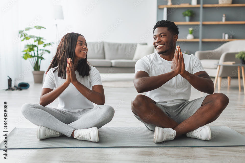 Fototapeta premium Keep Calm, Meditation And Healthy Lifestyle. Portrait of happy smiling young black couple holding hands in pray pose, keeping palms together, breathing and meditating, sitting on floor mat