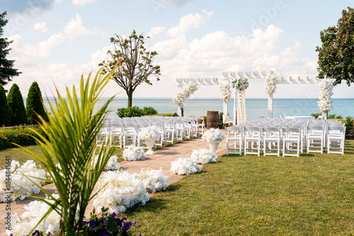 Photos Beautiful outdoor wedding ceremony setup by the sea with white chairs, floral ai