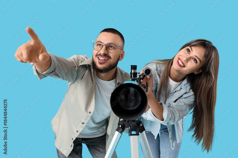 Fototapeta premium Young couple with telescope pointing at something on blue background