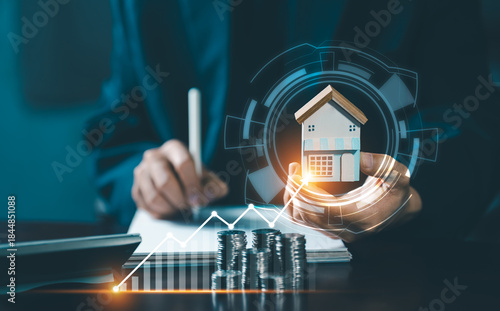 A person writing notes next to a calculator, with a miniature house and a line graph showing the rising value and potential for real estate investment and growth.