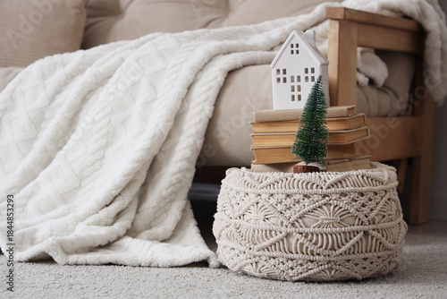Pouf with books, candleholder and Christmas tree near sofa in room