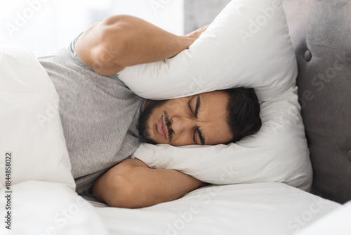 Tableau sur toile Middle Eastern man lies in bed, frustrated by loud noise