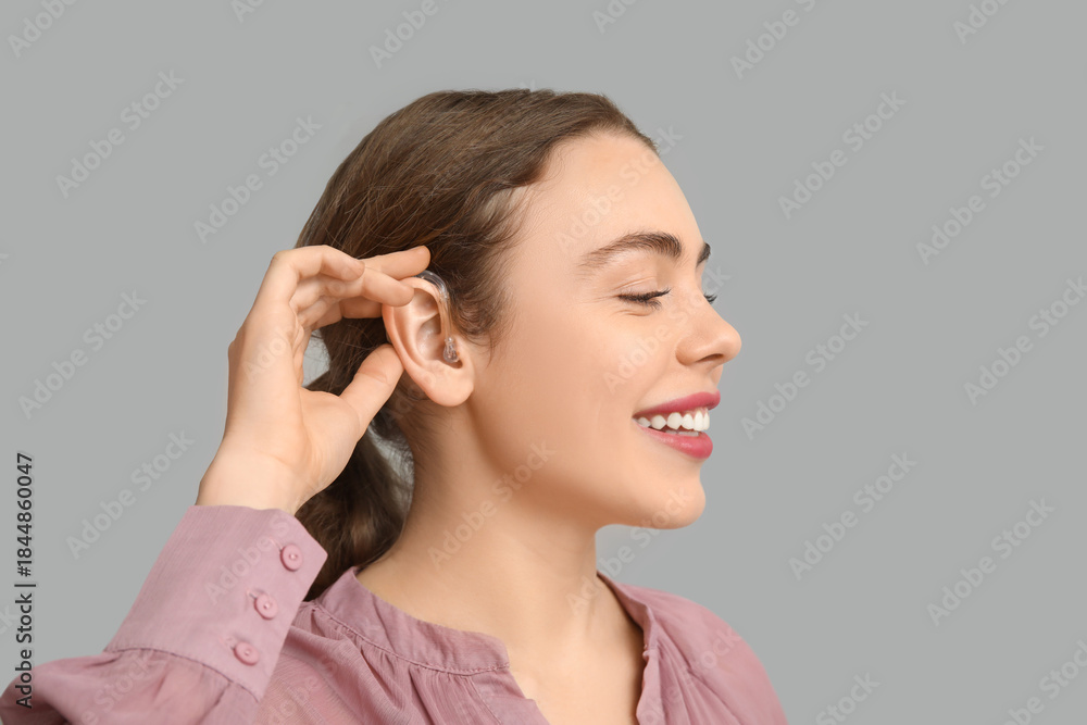 Fototapeta premium Happy young woman with hearing aid on grey background