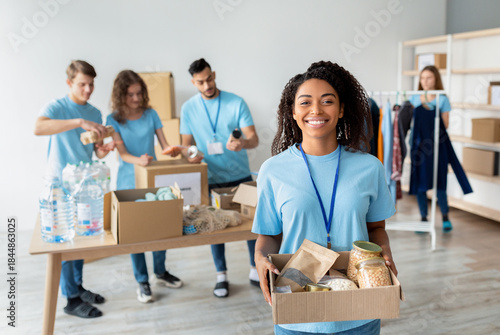 Fotografie A joyful african american female volunteer in a blue uniform holds a box of food donations
