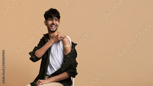 Obraz na płótnie A young man sitting on a chair smiles while rolling up his sleeve to display a bandage from a recent vaccination