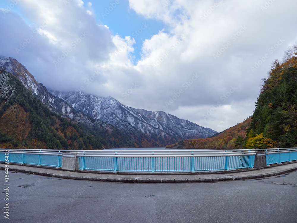 Fototapeta premium 観光名所立山黒部アルペンルートの黒部ダムのカラフルな紅葉と初雪の雪景色と散歩する外国人観光客の姿