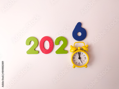 The image is a creative flat lay display of colorful numbers and a yellow alarm clock, used to represent the upcoming year 2026