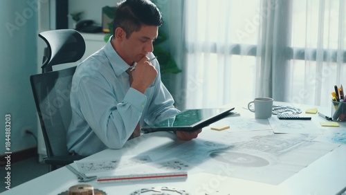 Fotografia Professional engineer looking at phone while working on tablet with green screen at meeting table with turbine engine or jet engine sketch design and various metal gear scatter around