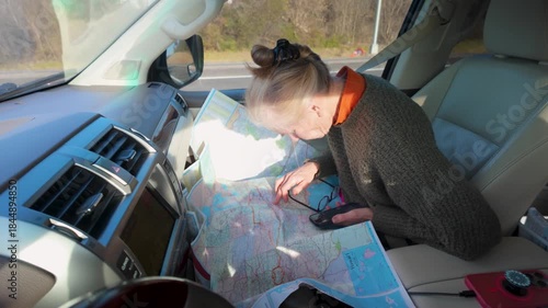 Mature woman studies a map and uses her phone to plan her journey while sitting in her camper vehicle.