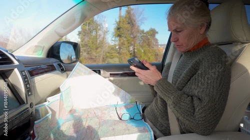 Mature woman sits in camper planning a trip using a map and phone while traveling down the road.