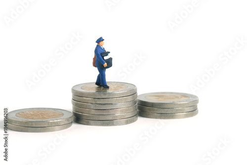 Miniature people toys conceptual photography. Cash on delivery and shipping cost service. Postman courier standing above money coin stack, isolated white background.