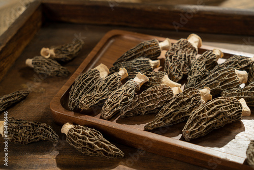 Close up of dried morel mushrooms, a gourmet culinary ingredient, on a wooden plate with a dark rustic background