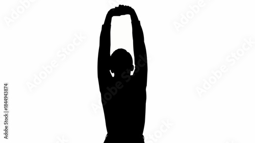 Silhouette of a person stretching arms overhead in a studio.