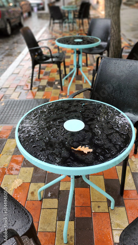 Empty tables and wicker chairs at a street cafe in the rain