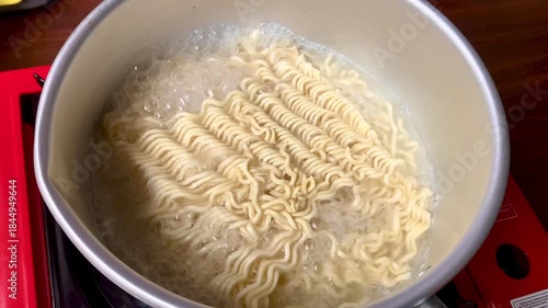 instant ramen noodles being cooked in boiling water in a metal pot