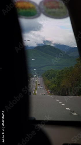 Vertical video. A Long Road leading toward Distant Mountains captured from inside a Vehicle in a First Person angle with Rolling Hills and Clouds, Scenic Journey Concept
